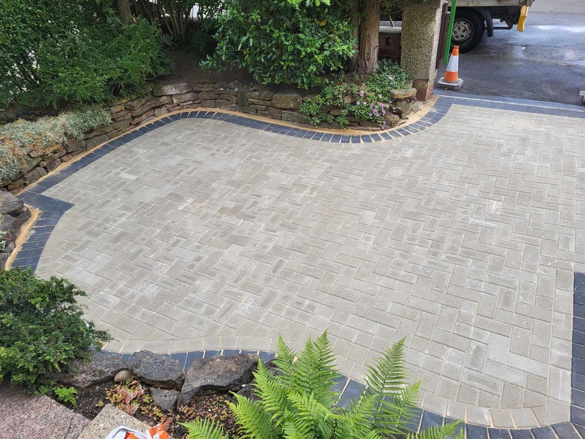 Light grey block paved driveway with a curved edge and planted border