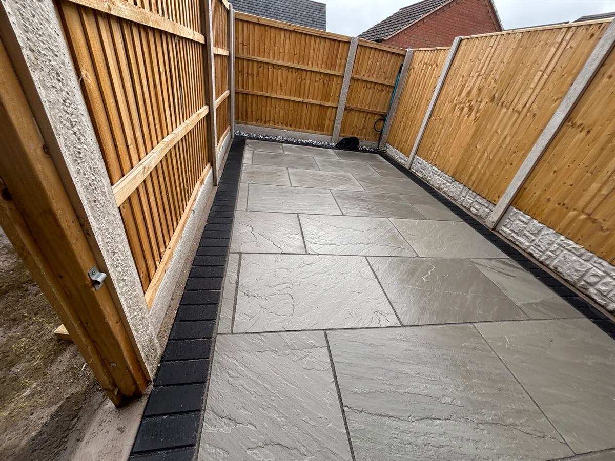 Sandstone patio with a charcoal border beside new fencing