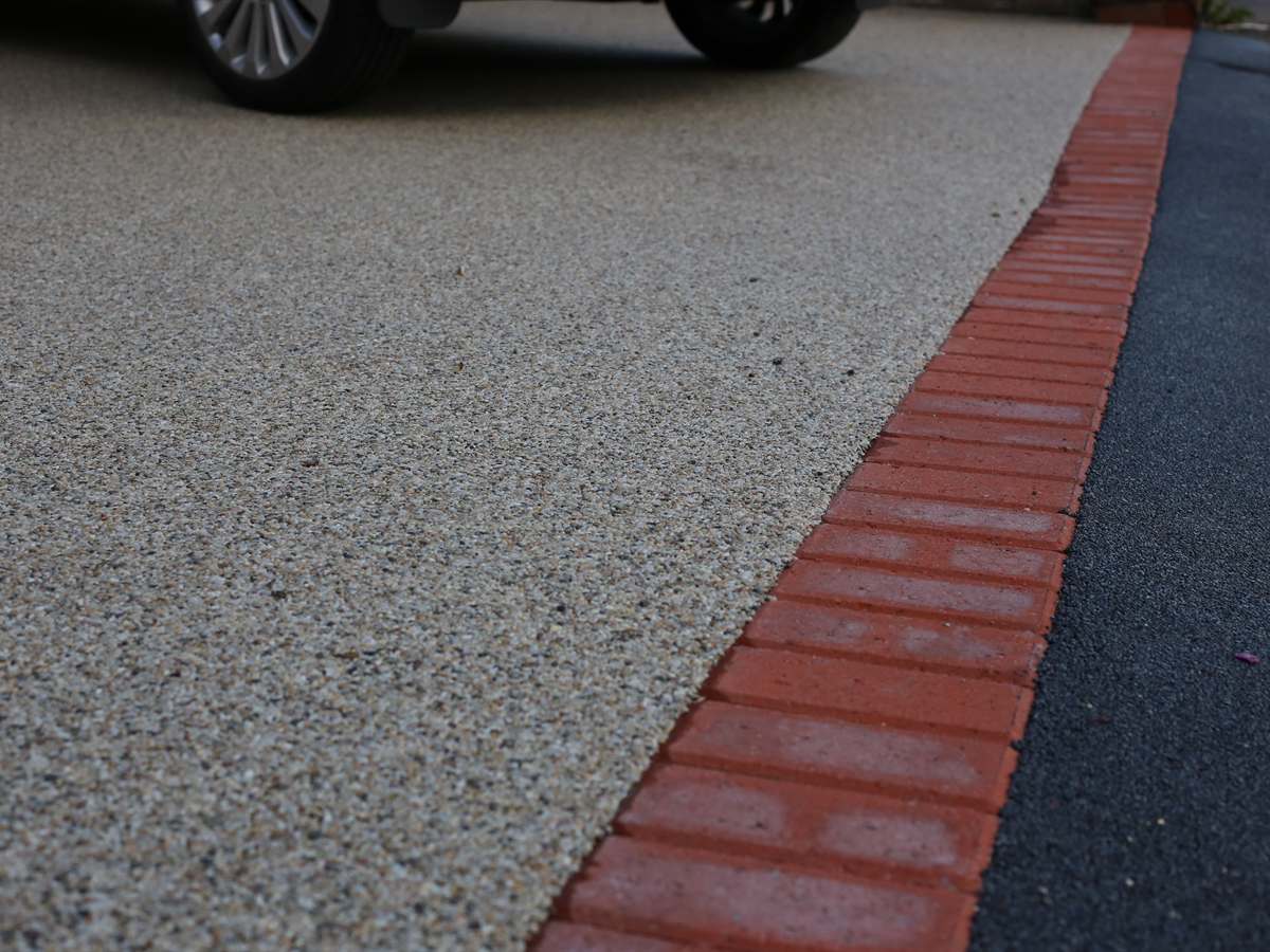 Resin bound driveway with a red brick soldier course edging against the road
